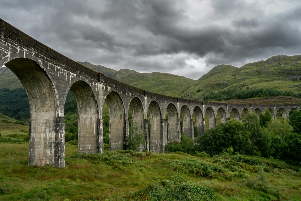 Stunning view of Glenfinnan Viaduct in Scotland, surrounded by lush greenery and dramatic clouds.